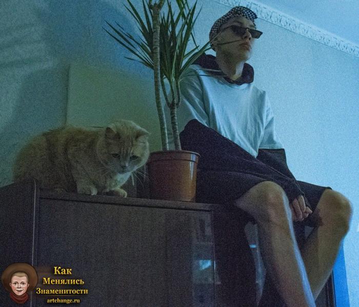 Мак Сима Мгла сидит с котом возле пальмы на столе